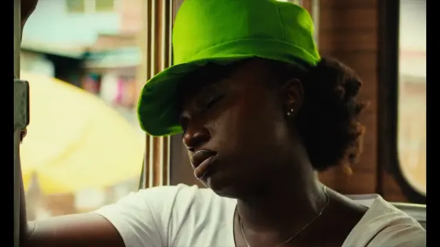Image du clip Faya : une femme en casquette verte, endormie contre une vitre